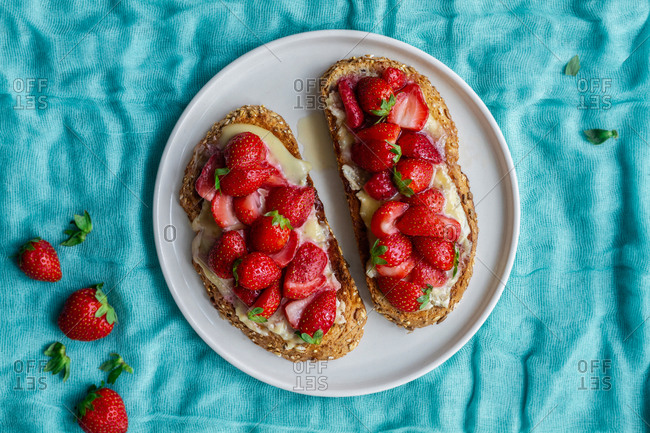 Top view of yummy sweet bread toasts with fresh chopped strawberries and honey served on plate on blue tablecloth