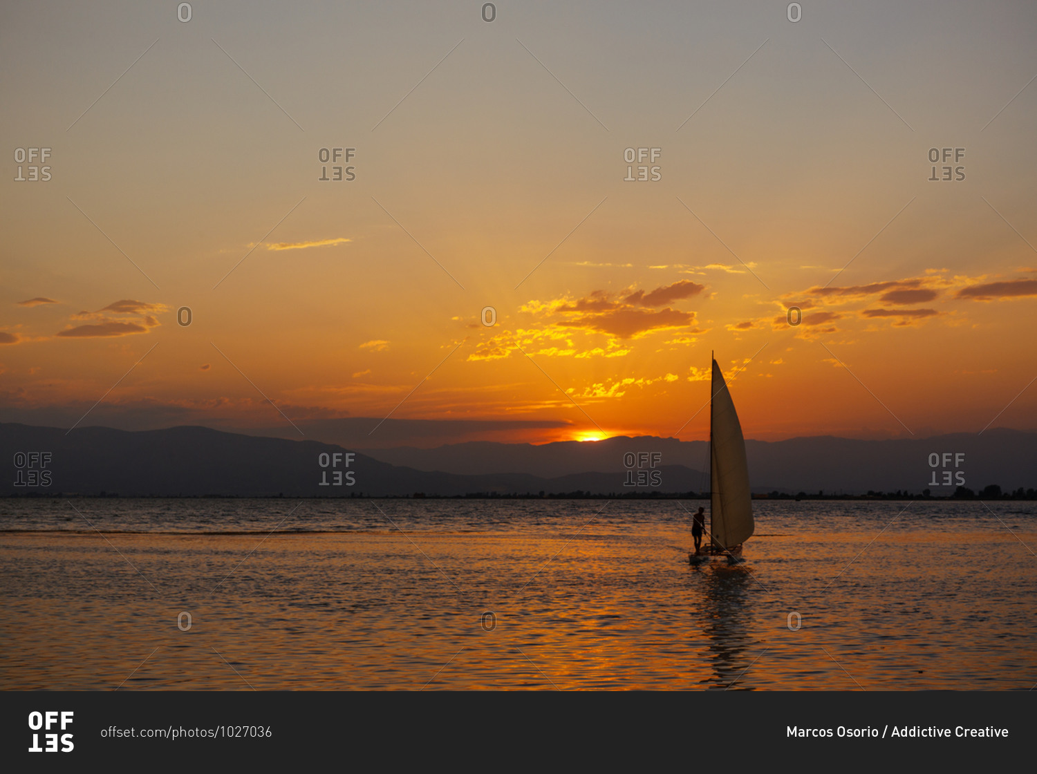 Little sailing boat in the sea at sunset with the sun and clouds in the background. Sailing on a summer adventure in the Mediterranean sea