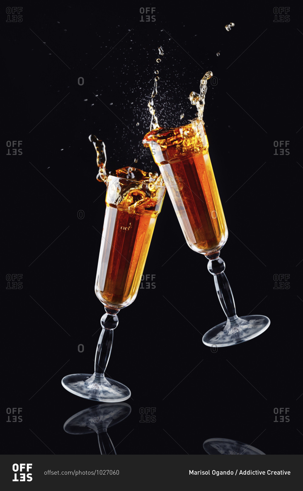 Crystal clinking glasses with splashing alcohol beverage on black background in modern studio