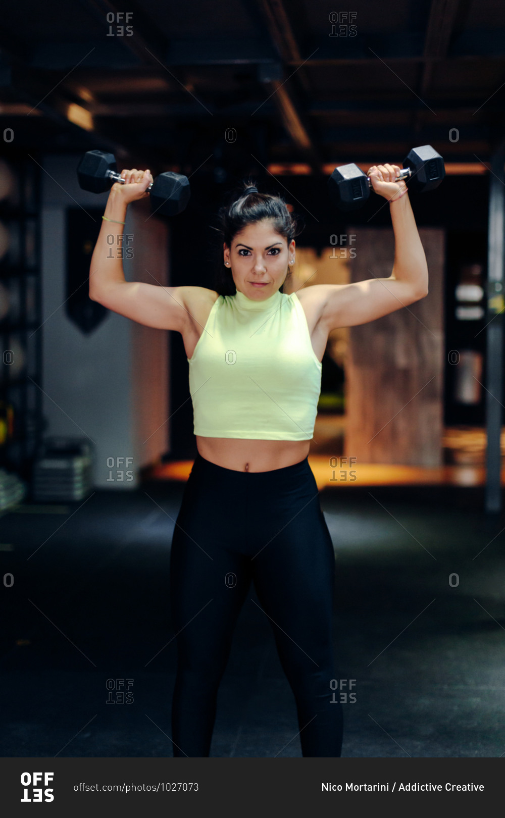 Full body of powerful muscular female athlete in sportswear doing exercise with dumbbells while training in modern gym