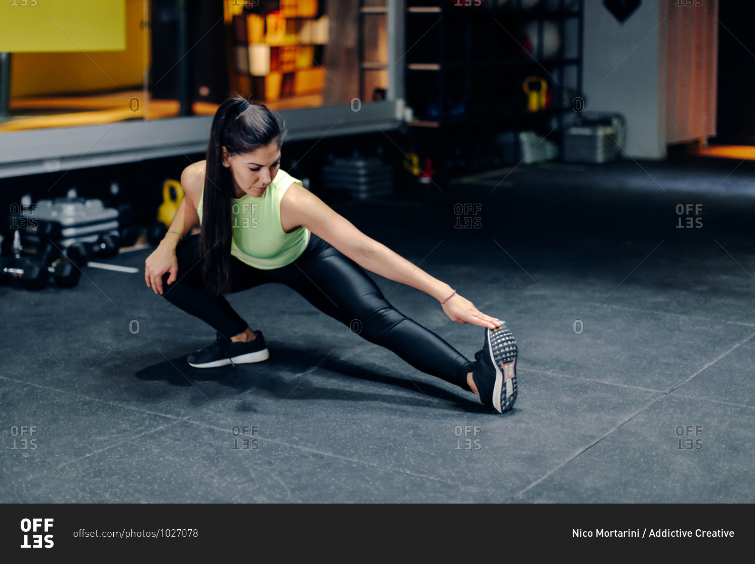 Full body female athlete in sportswear doing stretching exercise while training in modern gym