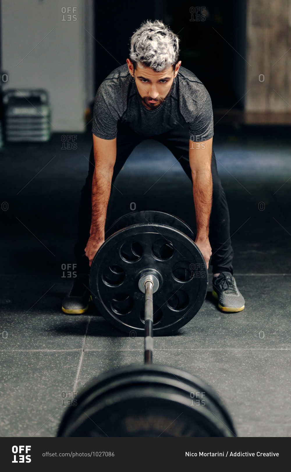Male athlete in sportswear putting heavy plates on barbell while preparing for weightlifting workout in gym