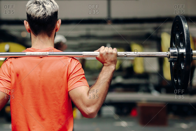 From behind crop view of male athlete lifting heavy barbell during intense workout in contemporary sports club