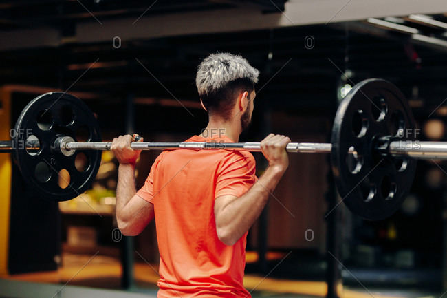 From behind view of male athlete lifting heavy barbell during intense workout in contemporary sports club