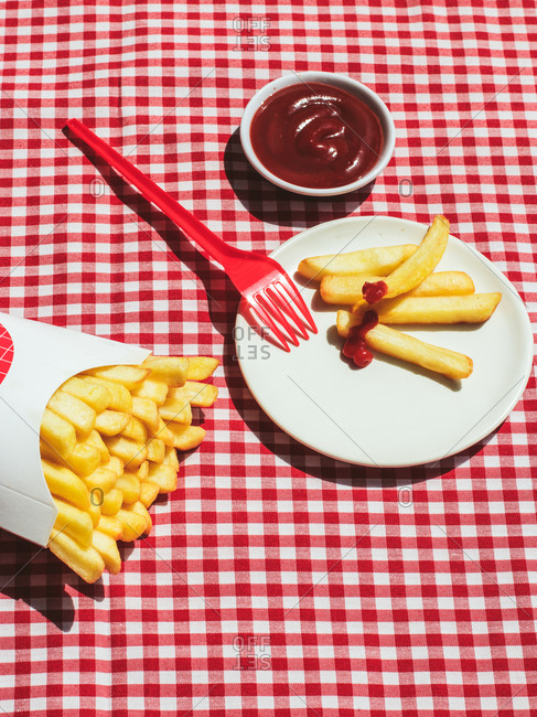 From above french fries packet near plate with potatoes soaked in ketchup