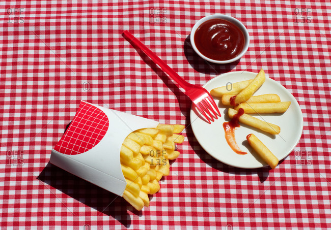 From above french fries packet near plate with potatoes soaked in ketchup