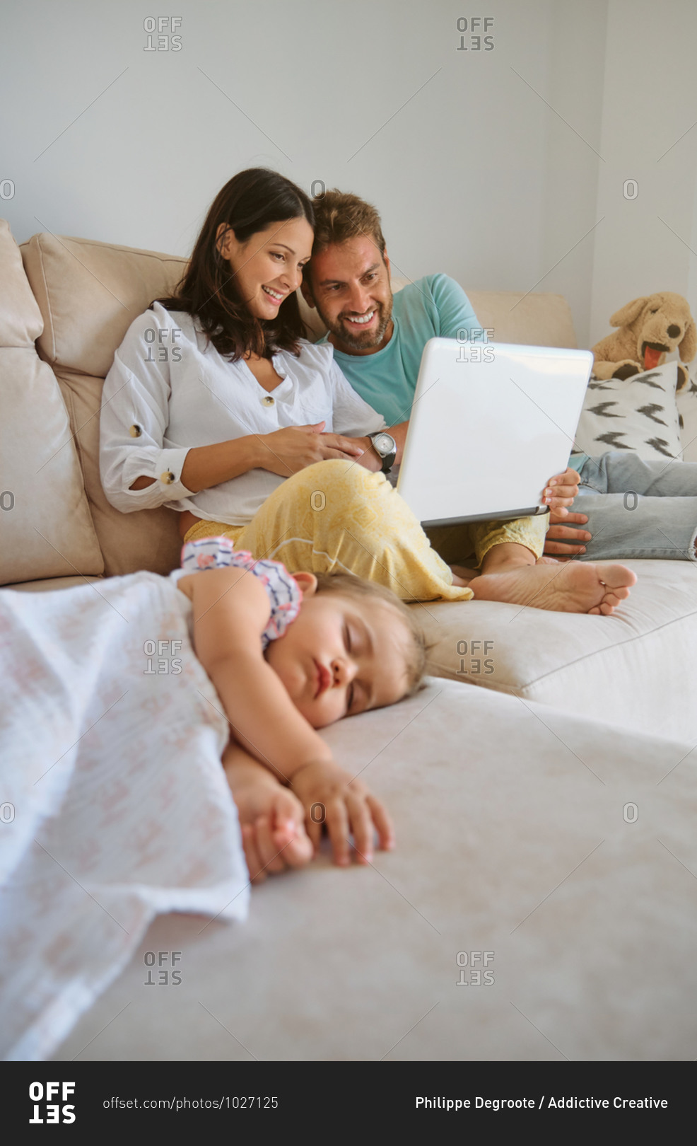 Little girl sleeping on the couch while a couple looks at the laptop next to her at home