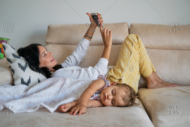 Little girl sleeping on the sofa covered with a blanket with her mother making a selfie lying next to it
