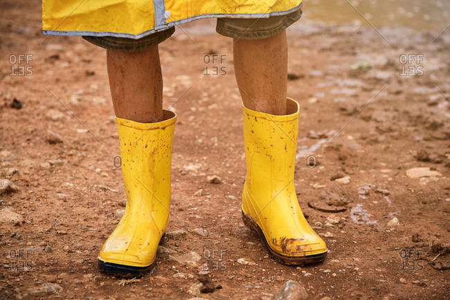Detail of some legs with yellow dirty muddy water boots in the middle of a path in the forest