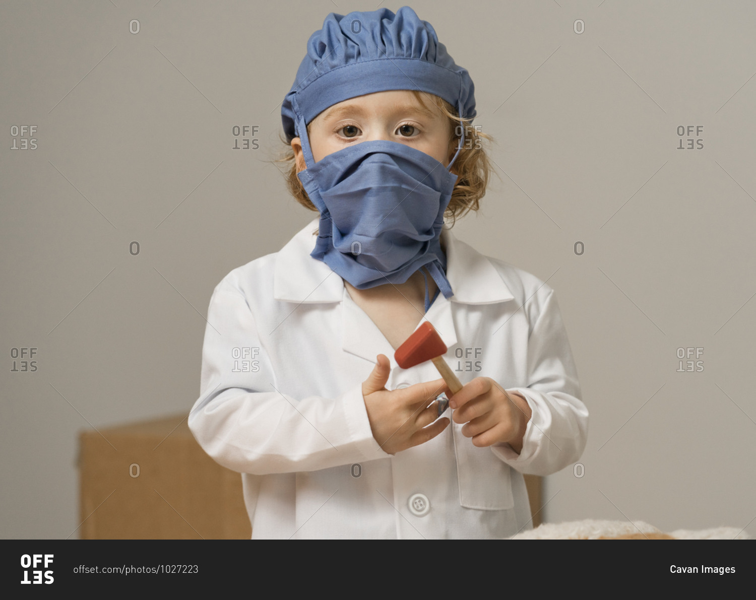 Young child in medical PPE holds a reflex hammer