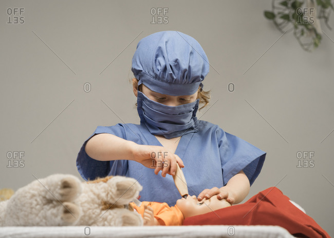 Young child wearing medical PPE examines a baby doll by checking it's temperature with thermometer