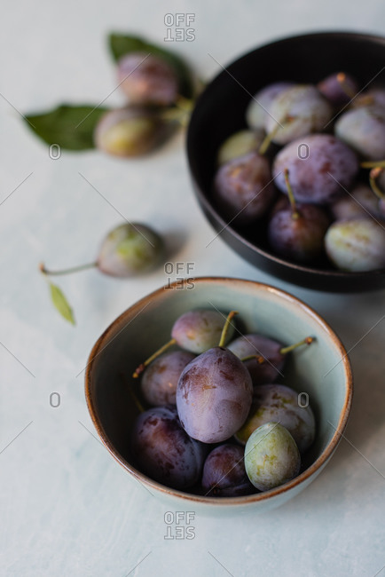Close up of bowls of fresh plums against a marble background.