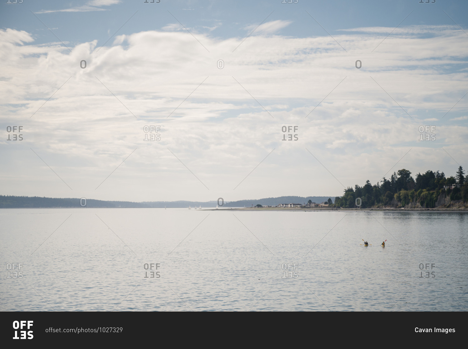 Two kayakers paddle across the water under a blue sky with white clouds near Port Townsend, WA
