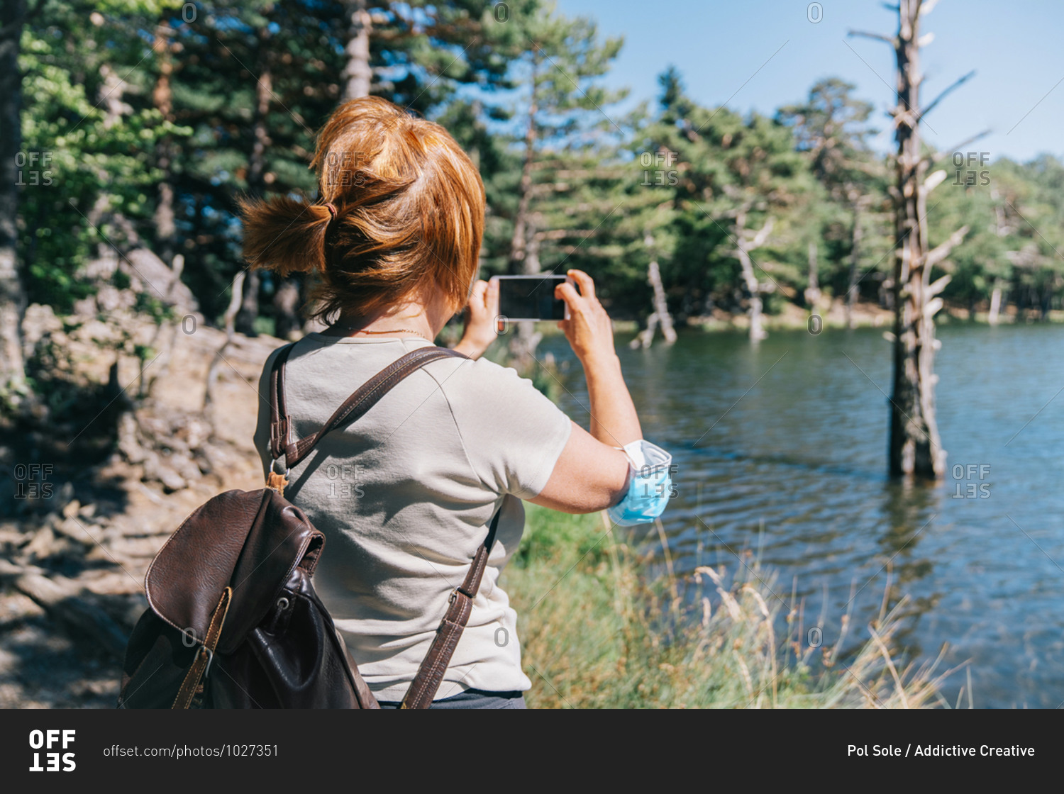 Mature woman with a medical face mask taking a photo with a mobile phone to a lake