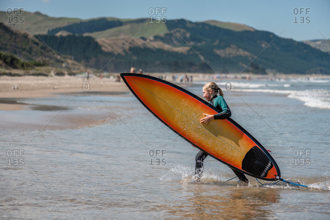Tween girl carrying a surfboard in New Zealand