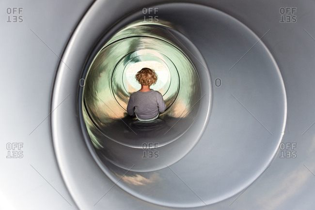 Young curly haired child in a tube slide at a playground park