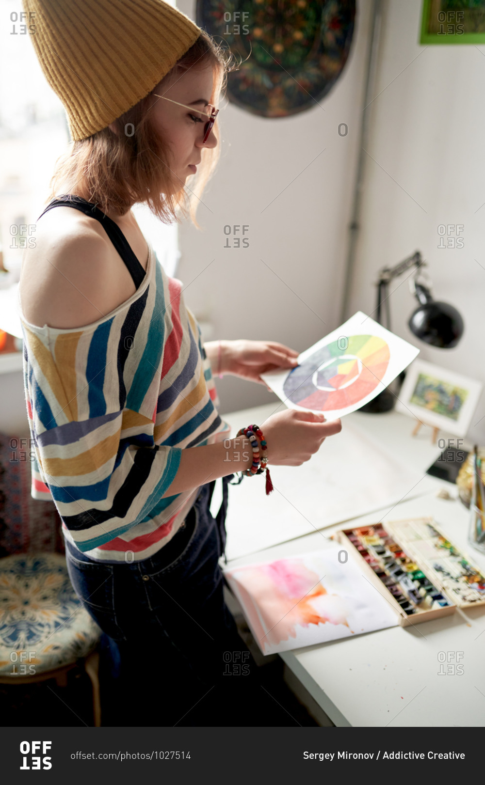 Side view of female artist standing at table with color wheel on paper while working on project in modern art studio