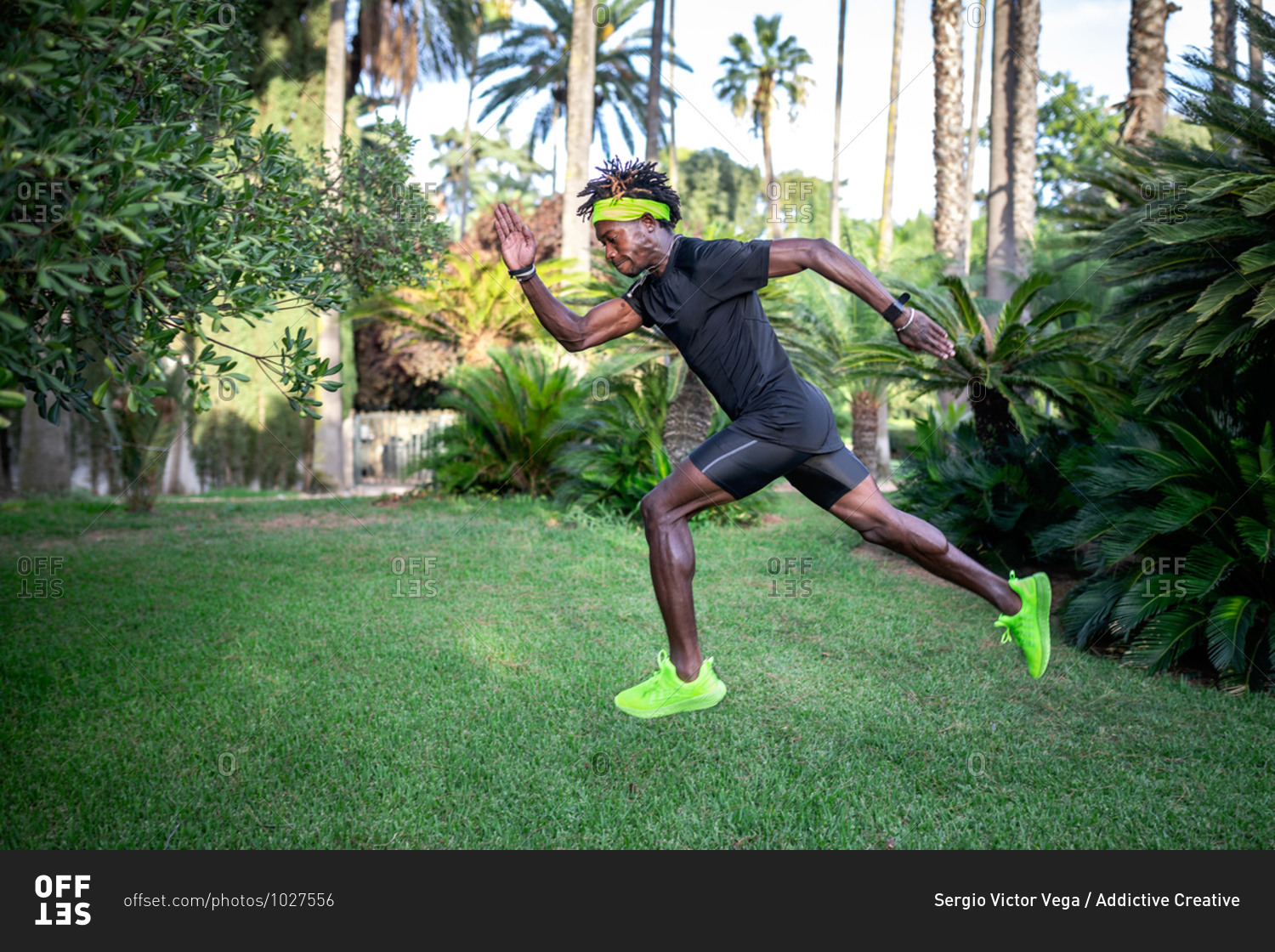 Side view of determined young African American male athlete in stylish sportswear running on green lawn in park