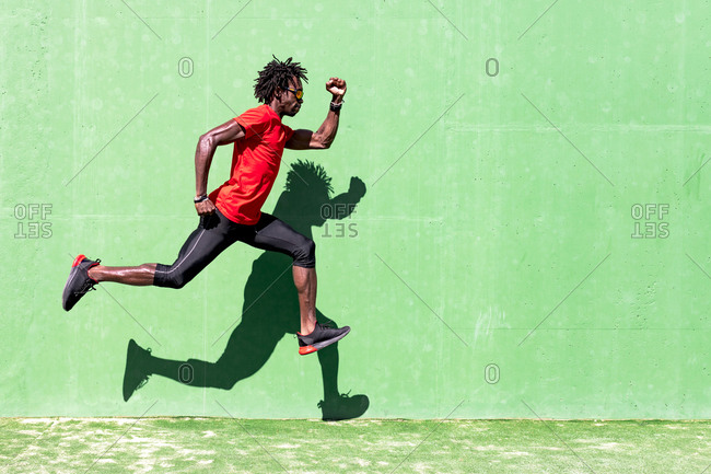 Side view of black sportsman in activewear in moment of jumping during intense workout on sunny day