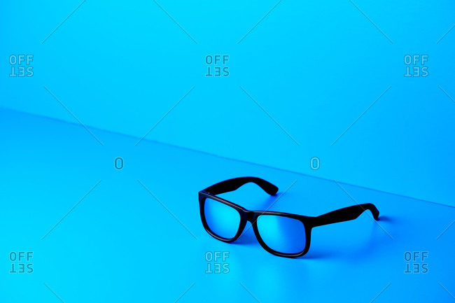 Trendy plastic glasses in black frame placed on table on blue background in modern studio