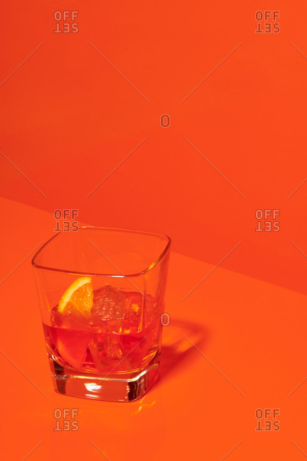 Crystal glass of alcohol drink with slice of lemon and ice cubes placed on table in studio on orange background