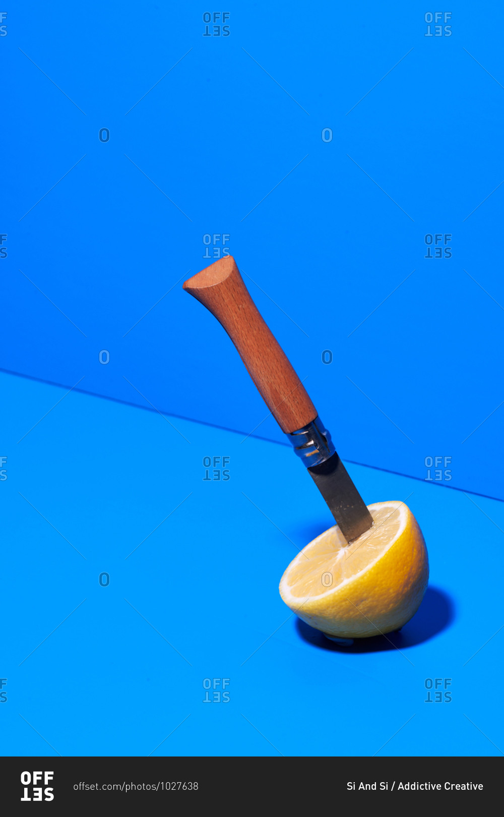 Half of ripe lemon with sharp knife placed on blue background in studio