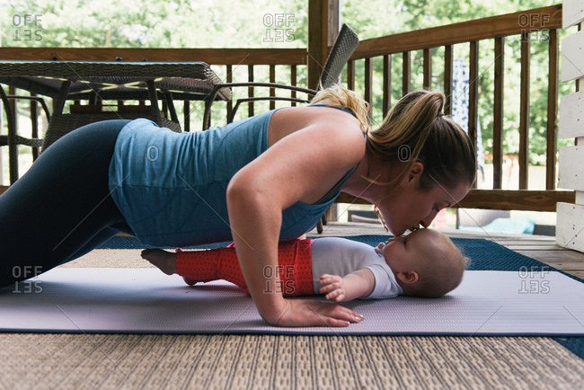 Mother kisses baby daughter while doing fitness routine at home