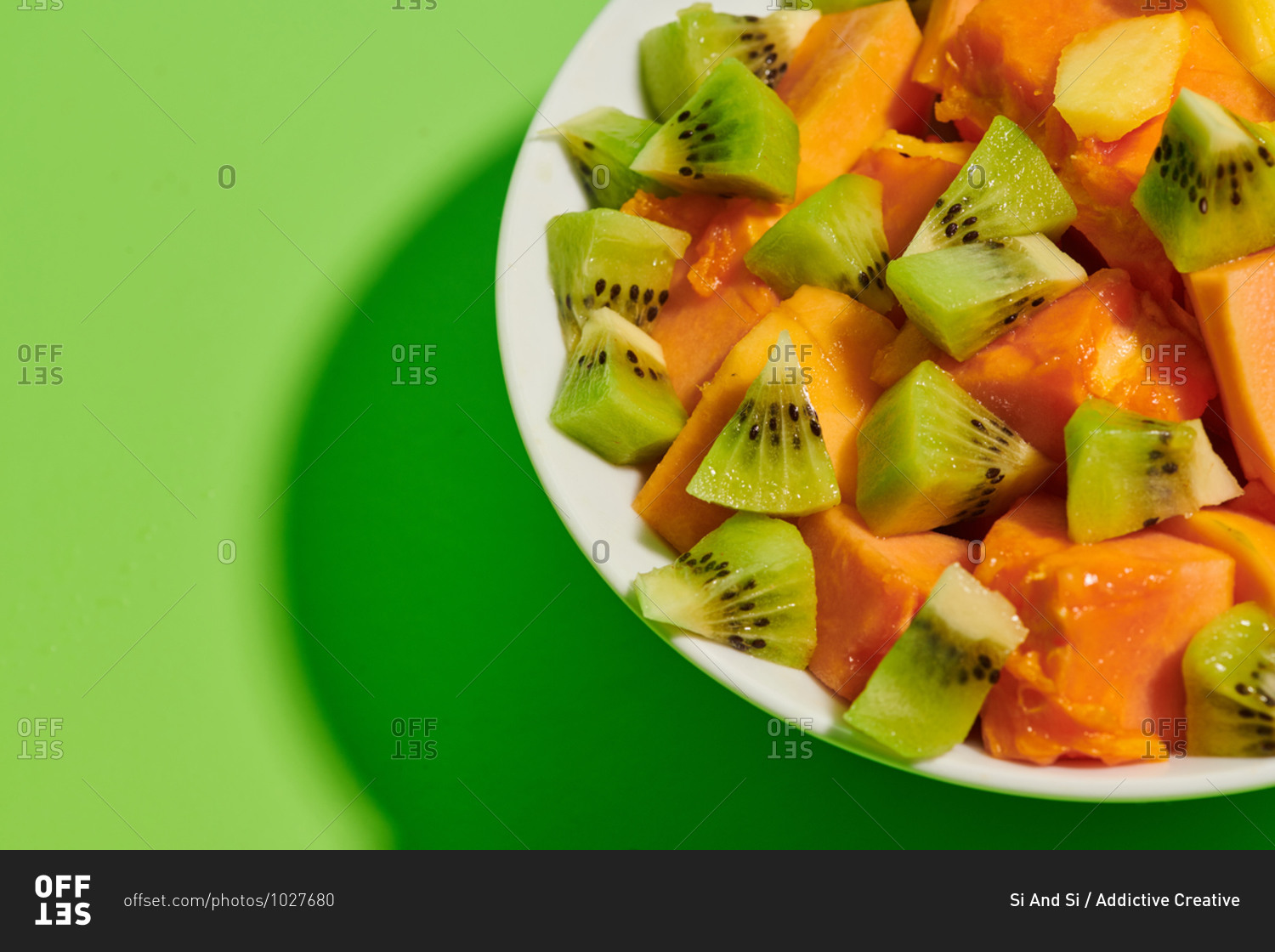 Closeup of delicious healthy natural fruit salad with chopped papaya and kiwi served in plate placed on bright green background