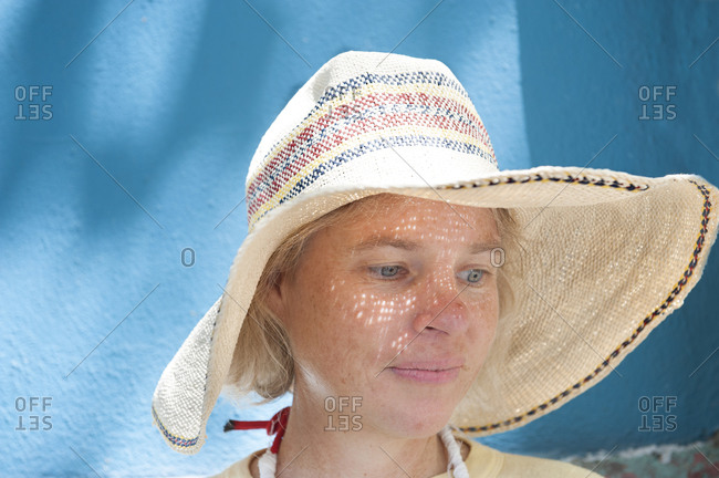 Delighted middle aged female wearing hat and standing near blue wall on sunny day during city stroll