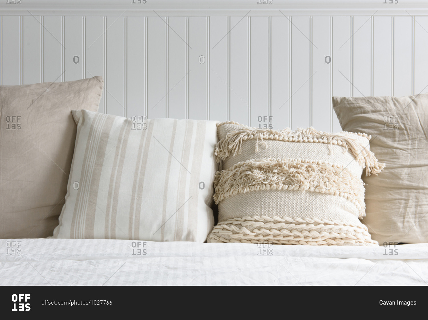 A collection of white and cream pillows on a bed with wood headboard