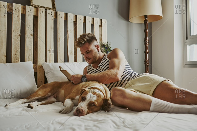 A young blond boy reading in bed with his dog