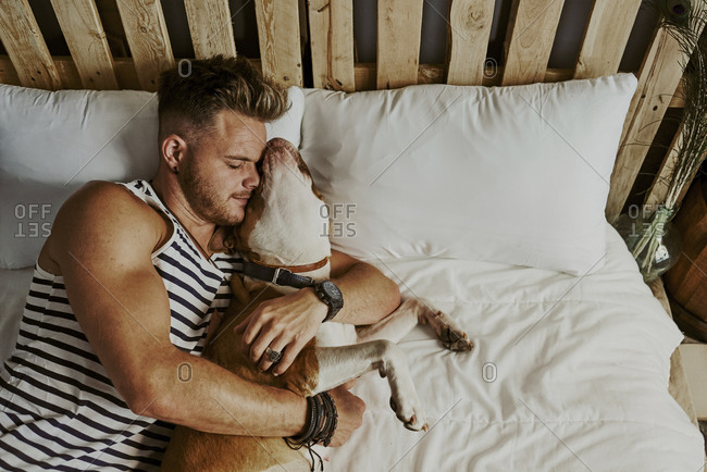 A young blond boy sleeping next to his dog in the bed