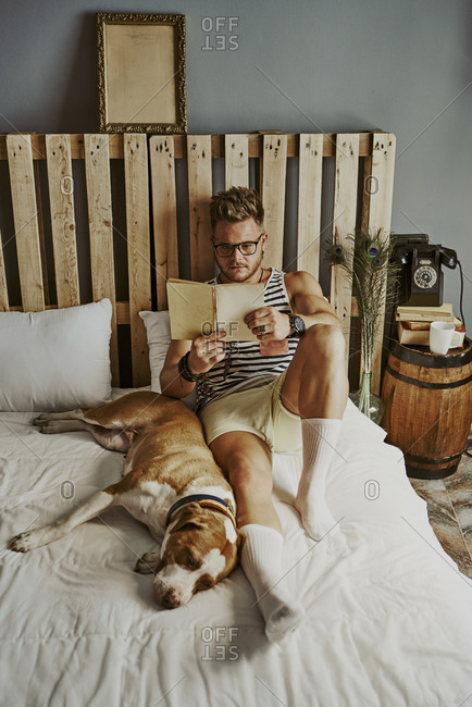 A young blond boy reading in bed with his dog