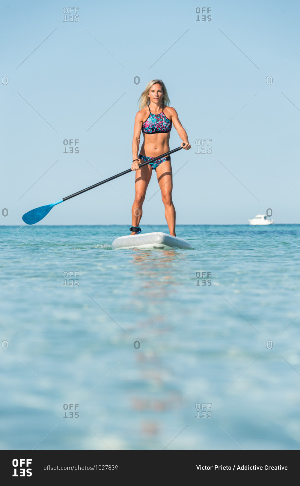 Fit female surfer in bikini standing on paddleboard and rowing while training in sea on sunny day