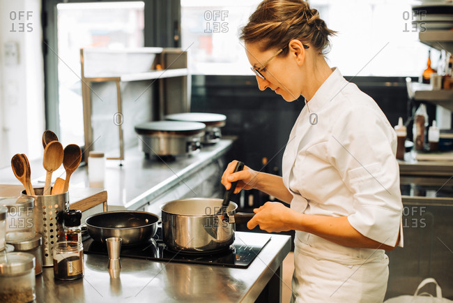 Female chef working in restaurant kitchen, stirring hot food in pan