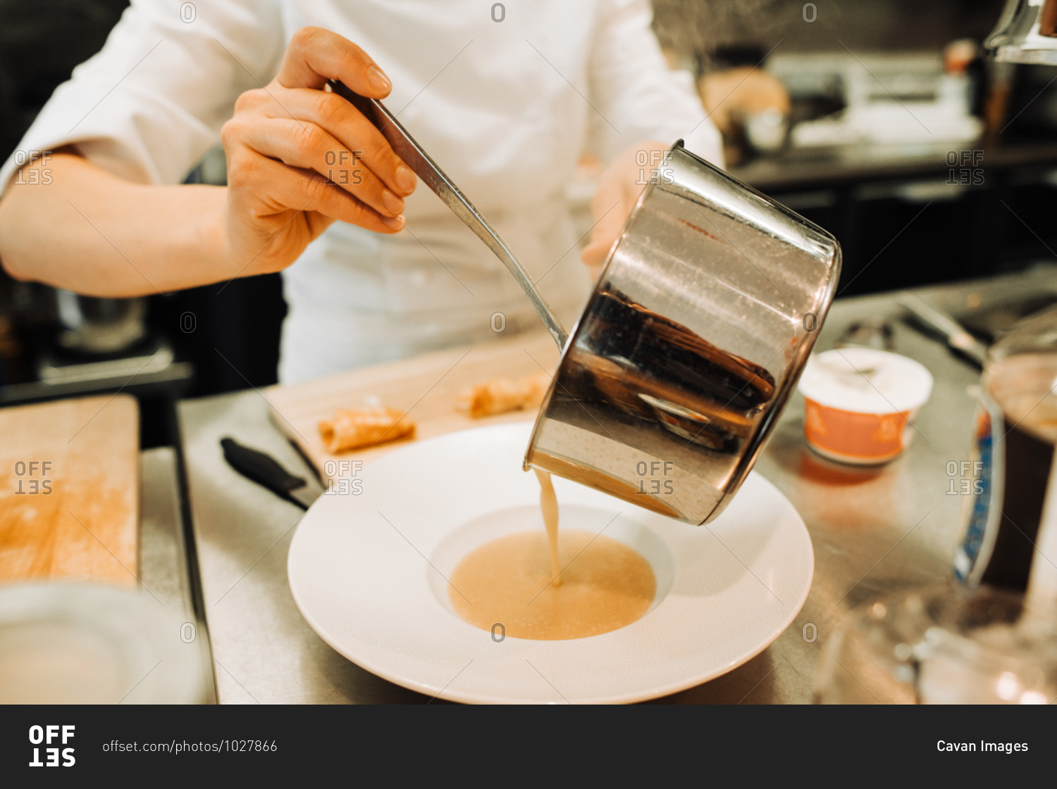 Chef pouring soup in plate while working in restaurant kitchen