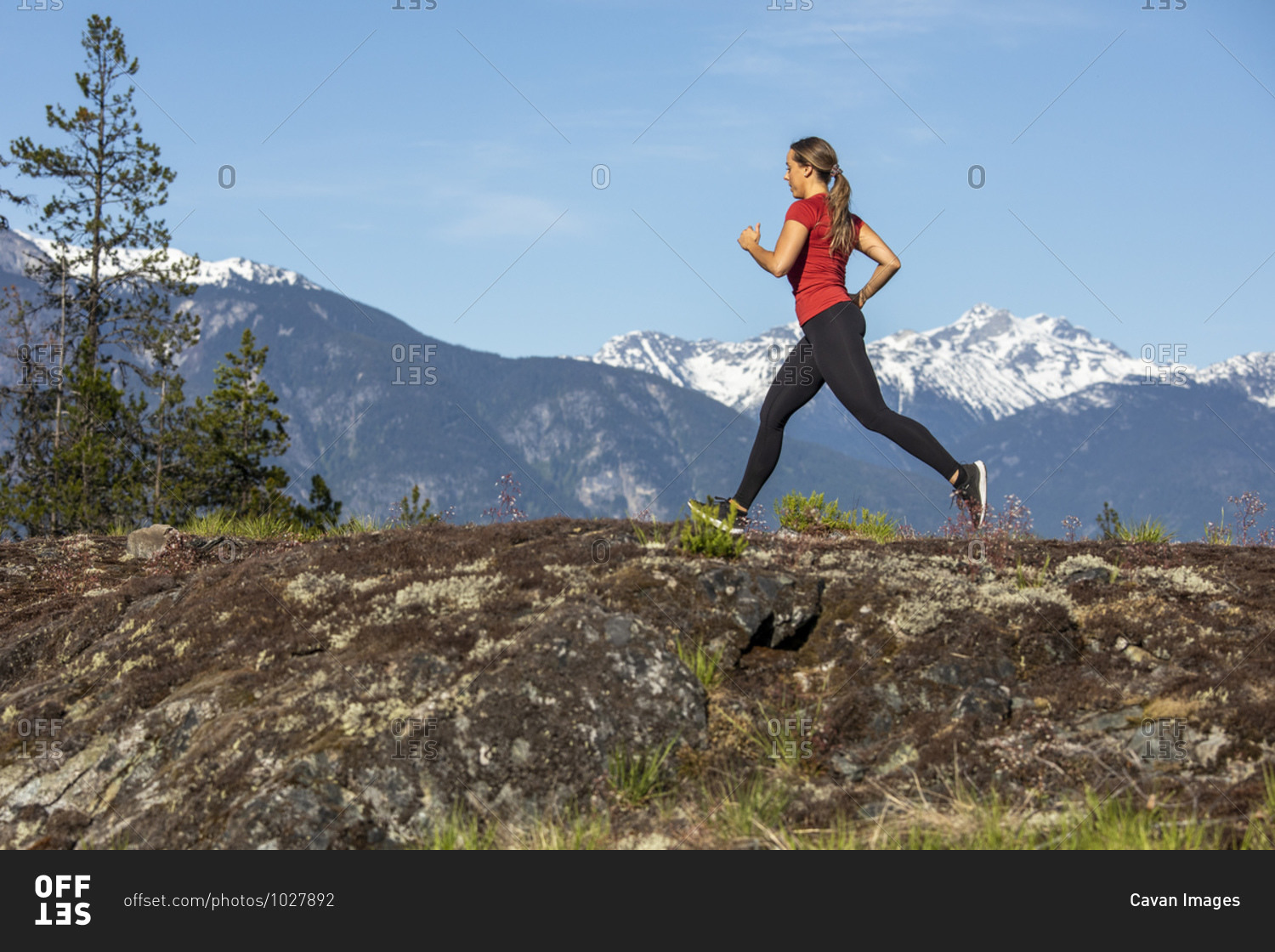 Side view of strong sportswoman running against snowy mountain ridge during fitness workout in countryside