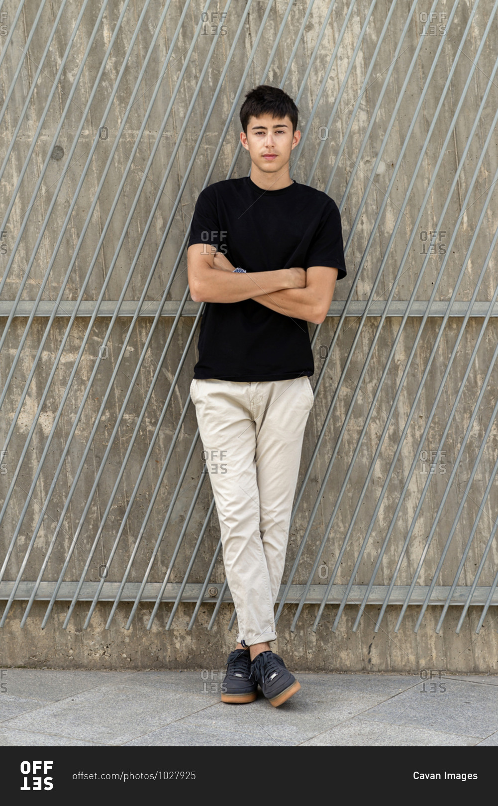 Young guy crossing arms leaning on wall, looking camera
