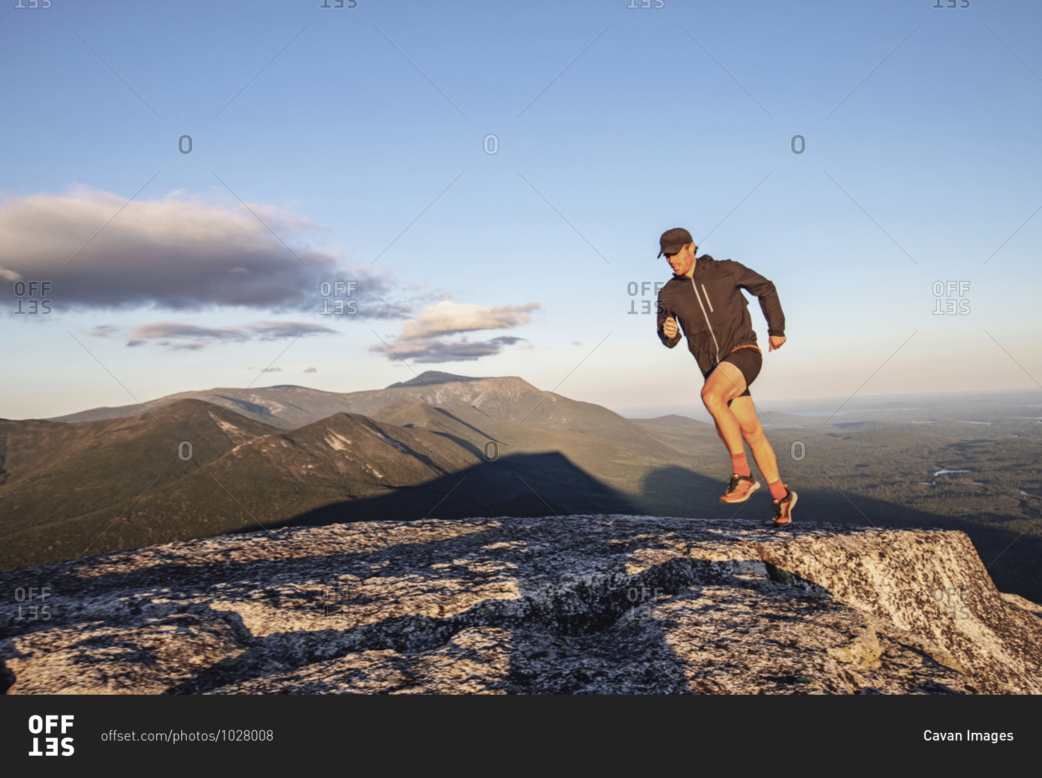 Fit male trail runner runs across rocks on summit of Doubletop, Maine
