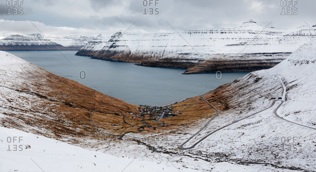 Breathtaking scenery of residential houses located near river in highland valley with mountains covered with snow on Faroe Islands