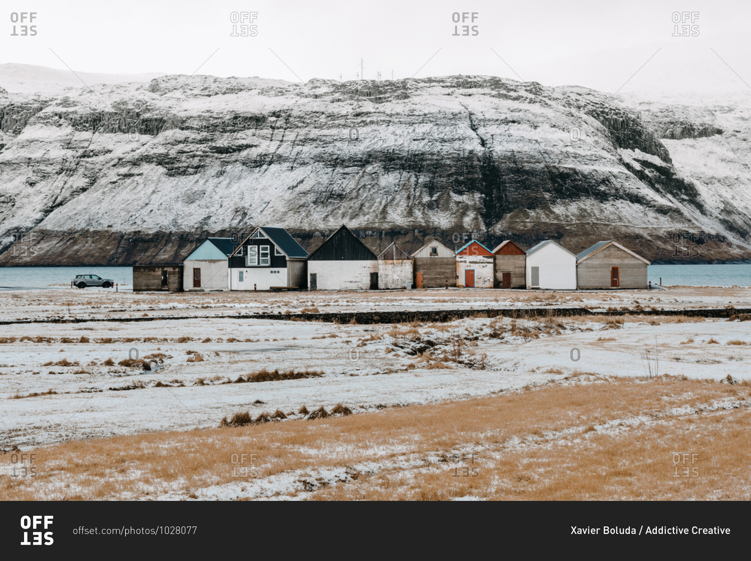 Breathtaking scenery of residential houses located near river in highland valley with mountains covered with snow on Faroe Islands
