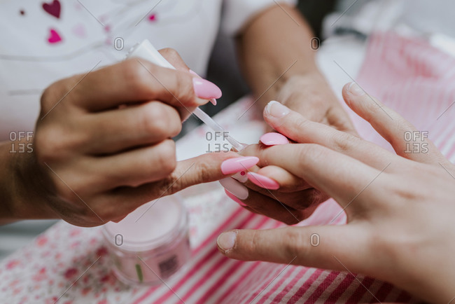 High angle of unrecognizable female artist applying nail polish on fingernails of client during manicure in beauty studio