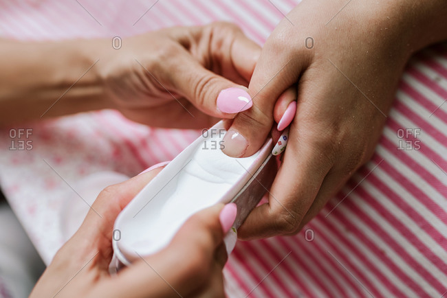 Unrecognizable female master doing manicure and putting nail of customer in glitter while working in beauty salon