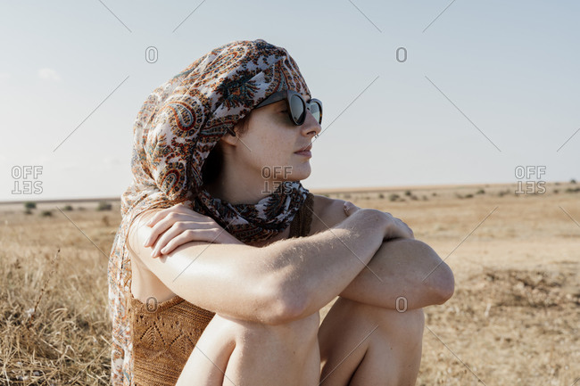 Portrait of young woman wearing headscarf and sunglasses sitting outdoors with crossed arms
