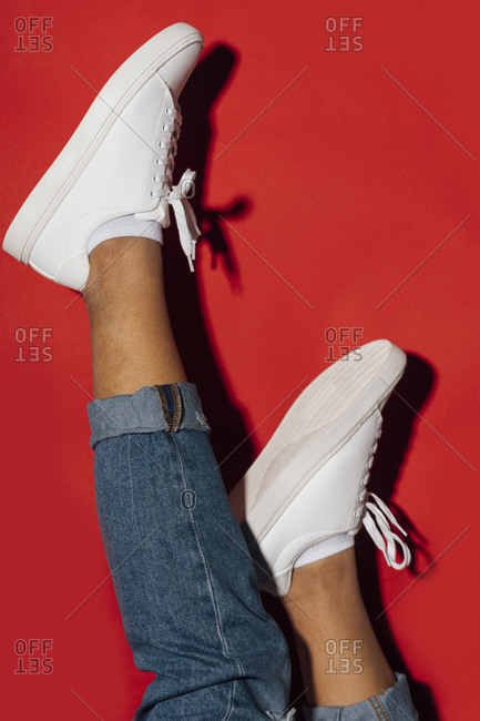 Close-up of woman wearing sneakers with feet up on red background