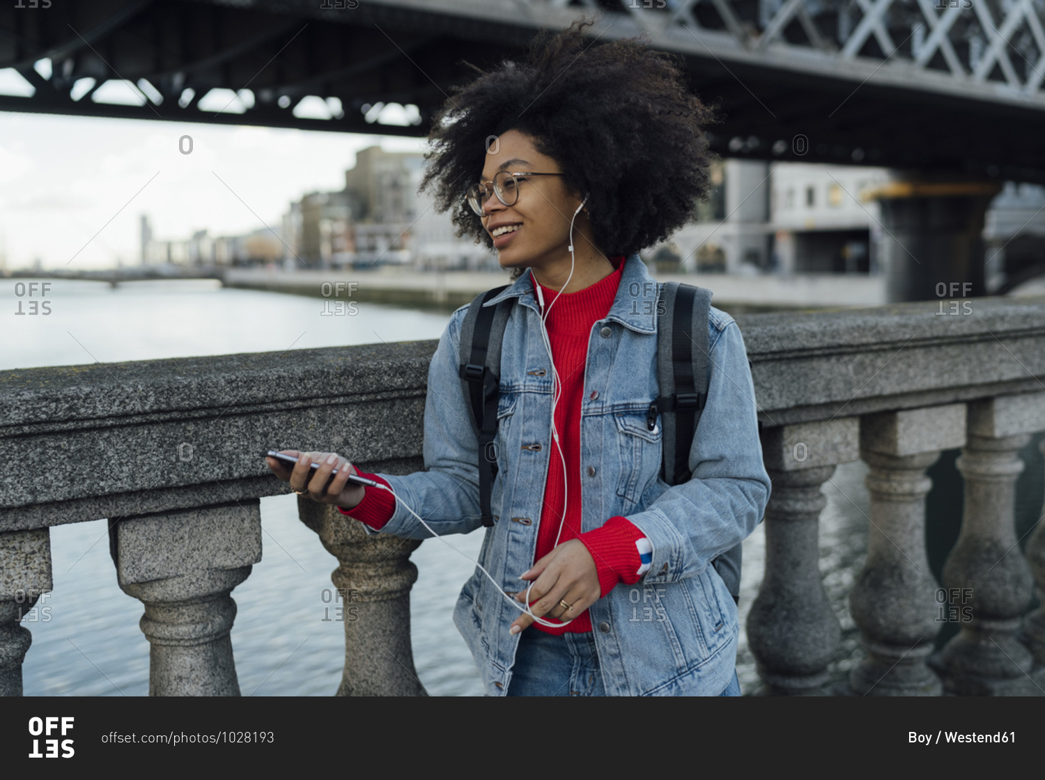 Afro young woman listening music through headphones while standing by railing on footbridge