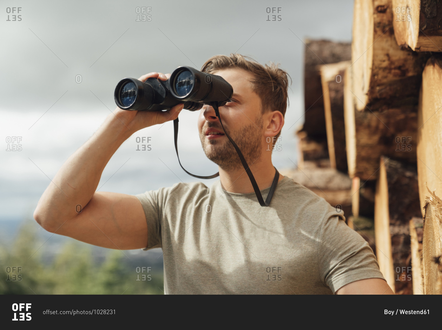 Mid adult man looking through binoculars against sky in forest