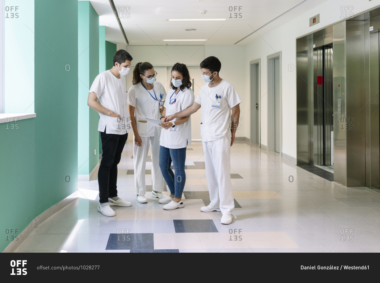 Doctors wearing surgical masks discussing over digital tablet while standing in corridor at hospital