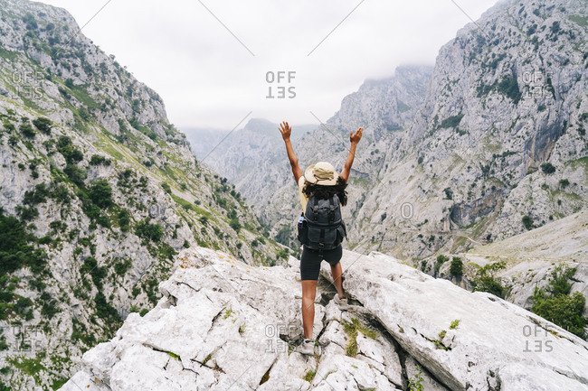 Carefree woman with hand raised standing on mountain peak at Ruta Del Cares- Asturias- Spain