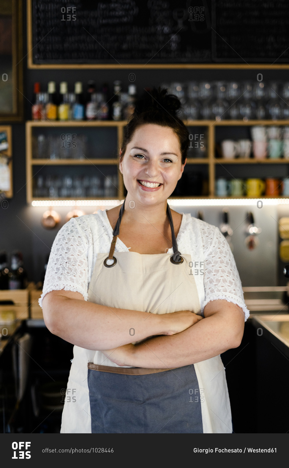 Smiling female owner with arms crossed standing in coffee shop